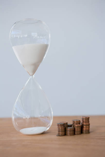 istock Hourglass and stacks of coins on table 653382706