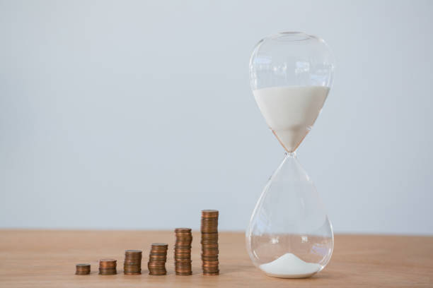 istock Hourglass and stacks of coins on table 653382780