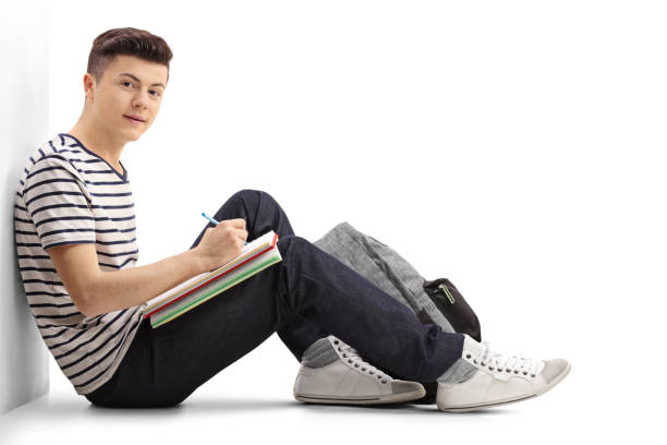 Teenage student leaning against a wall writing in a notebook
