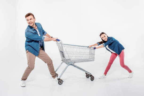 istock smiling couple pulling empty shopping cart and looking away on white 653456610