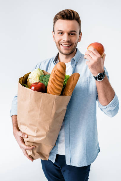 istock Handsome young man holding grocery bag and apple smiling at camera 653457206