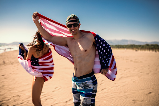 Guys and girls with American flags on the beach. Patriots of America. Young people having fun.