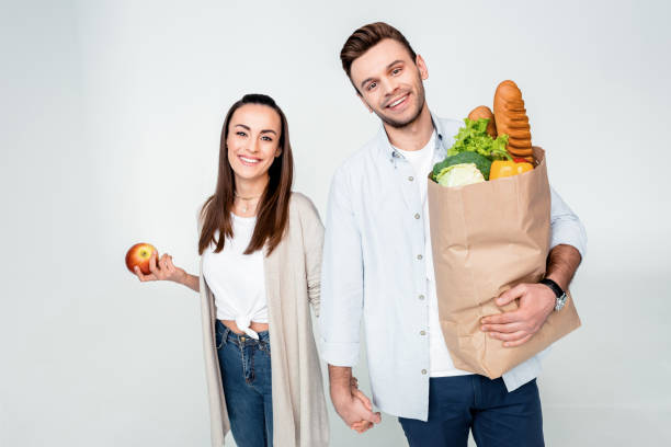 istock Happy young couple holding hands while standing with grocery bag and apple 653459786