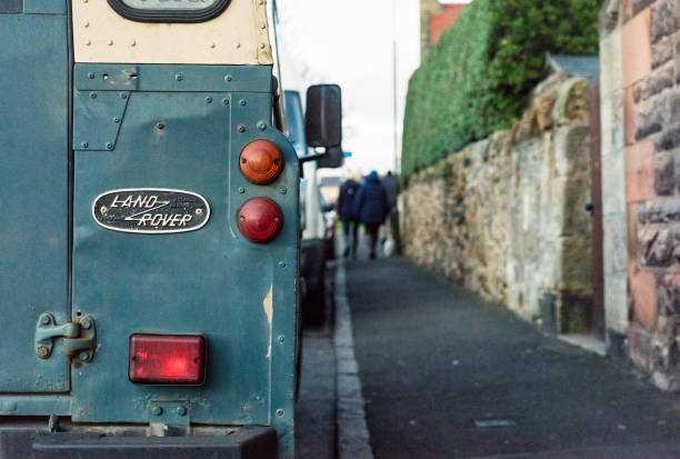 Gullane, Scotland, UK - Rear view of an old-fashioned Land Rover 4x4 vehicle, parked on a street, with pedestrians in the distance.