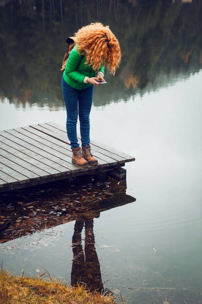 A woman hiker standing calmly on river stones, embodying serenity and connection as majestic mountains reflect in the tranquil water around her, New Zealand.