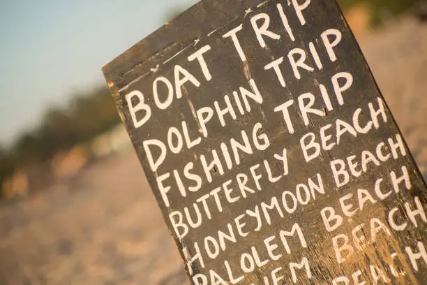 A board on the beach in sunset advertising dolphin trips and other diffrent boats trips