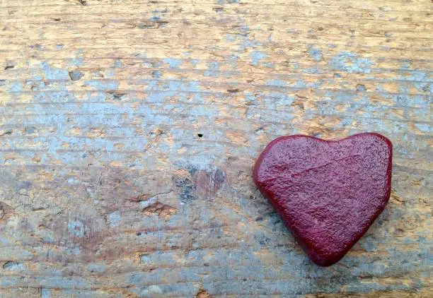 Lonely red heart made of stone on old wood