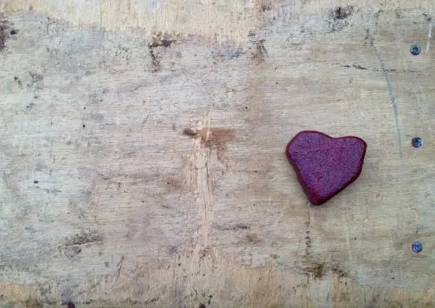 Lonely red heart made of stone on old wood