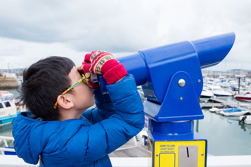 Young asian boy looking in telescope at harbor