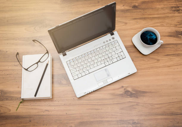 istock table with laptop, coffee and notebook on wooden table with sun beam.  Top view 653514256