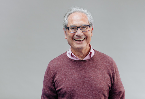 Portrait of a natural smiling, happy senior French businessman with glasses and smart casual, real people studio shot with copy space on gray background. XXXL