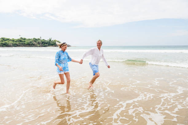 starszy mężczyzna i kobieta biegający w morzu trzymając się za ręce - beach couple satisfaction playing zdjęcia i obrazy z banku zdjęć