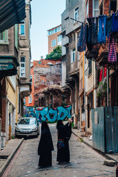 Two young woman dressing black scarf taking pictures with smart phone on narrow medieval street view in Balat, Fatih, Istanbul