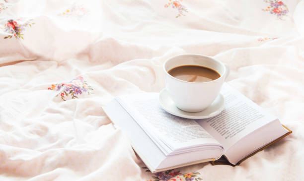 istock Still-life coffee cup and a book in bed on floral bed sheets 653539250