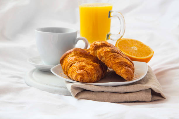istock Bed breakfast with coffee cup, croissants and orange juice on white sheets 653539356