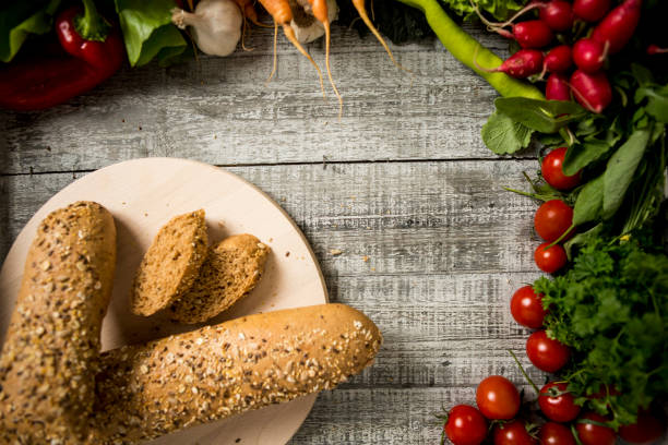 Freshly baked bread is cut into pieces on the board surrounded by fresh vegetables