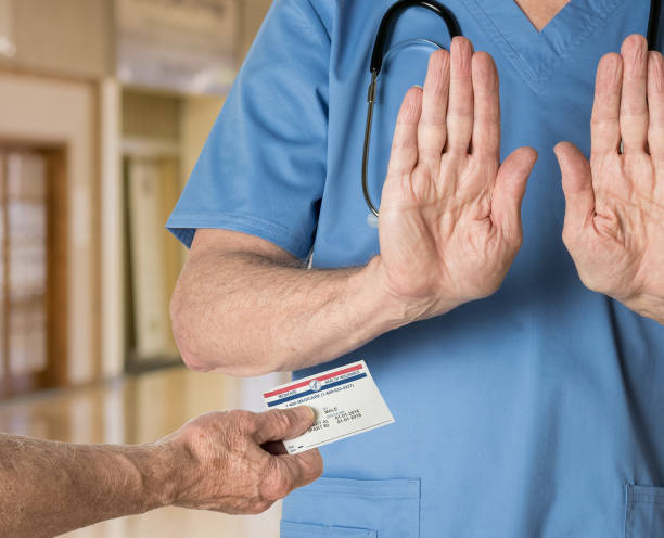 Senior doctor in scrubs refusing Medicare Card Senior caucasian doctor in scrubs in hospital refusing to treat a patient with a Medicare card hospital card stock pictures, royalty-free photos & images