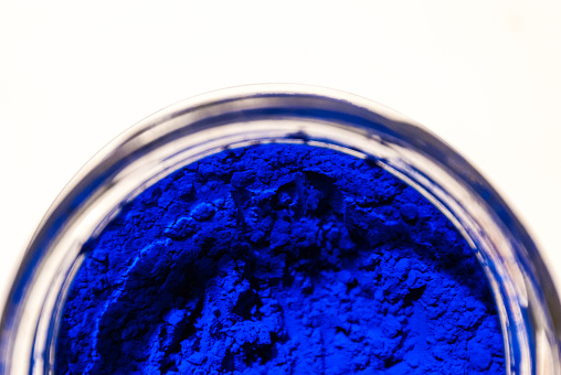 Close-up shot of blue powder pigment in a glass pot on white background