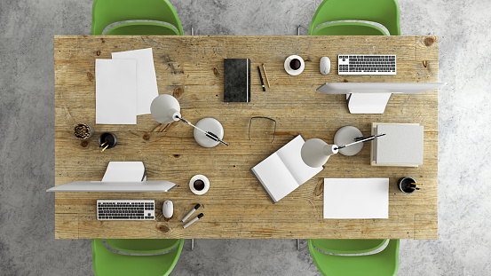 Business group scene showing overhead office desk with multiple chairs around, corporate teamwork template. laptop, tablet, PC computer monitor keyboard, notepad, paper, green chairs around. no people