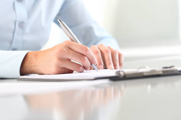 istock Woman's hands writing on sheet  in a clipboard with a pen; isolated on desk 653752914