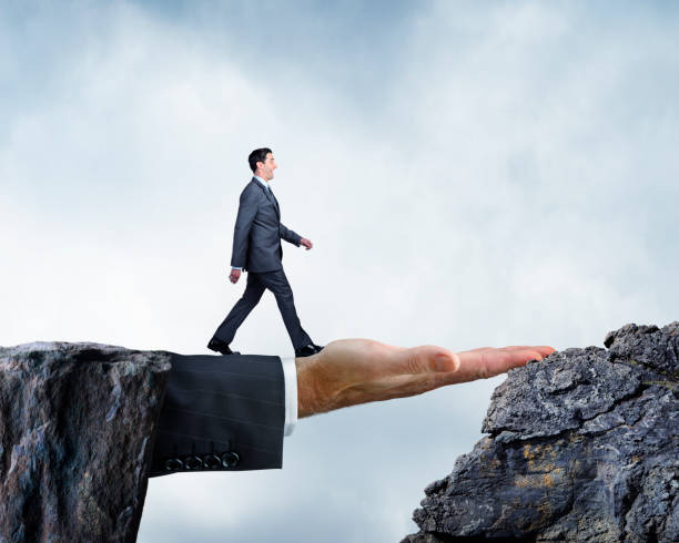 istock Businessman Walking Across Bridge Created By Large Hand 653763678