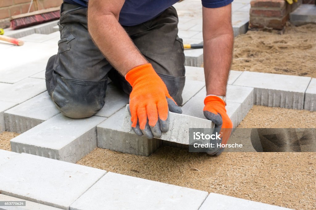 Hands of a builder laying new paving stones. Hands of a builder laying new paving stones carefully placing one in position on a levelled and raked soil base. Paving Stone Stock Photo