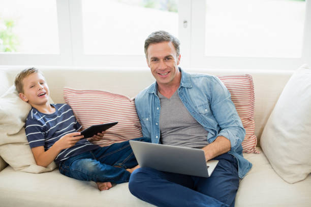 istock Father and son using laptop and digital tablet in living room 653771020