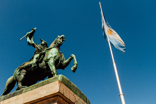 Statue of Manuel Belgrano and Argentine flag in the Plaza de Mayo of Buenos Aires. Bronze equestrian sculpture created by Albert-Ernest Carrier-Belleuse and Manuel de Santa Coloma. Inauguration: September 24, 1873. Location: Plaza de Mayo, Buenos Aires, Argentina. The sculpture was inaugurated during the presidency of Domingo Faustino Sarmiento, by order of the Presidency of the Nation. It is located in front of the government palace (Casa Rosada) next to the Argentinean flag