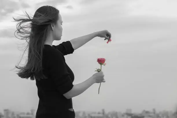 Photo of A beautiful lonely woman hoping for love in front of a city view, playing he loves me, he loves me not