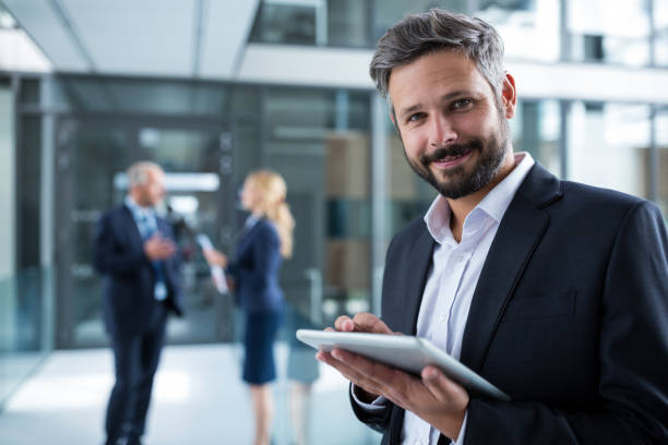 Businessman using digital tablet in office corridor Portrait of businessman using digital tablet in office corridor sales executive stock pictures, royalty-free photos & images