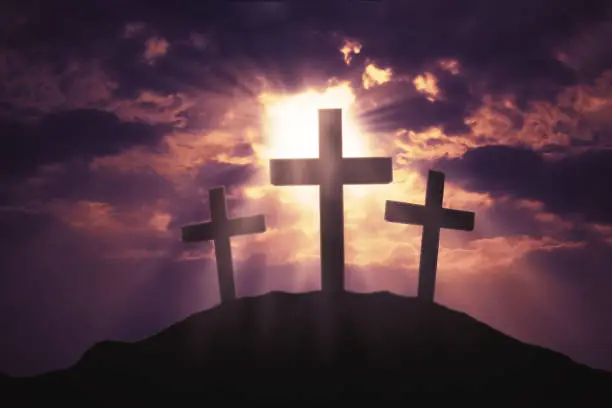 Image of three christian crosses symbol on the hill with bright sunlight on the sky at sunset time