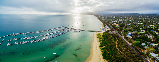 Aerial panorama of land and sea. Long pier and yachts moored at marina near the beach