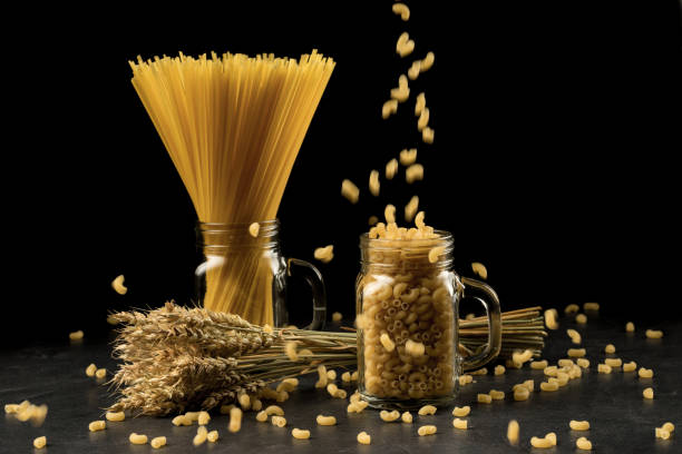 grappolo di grano, maccheroni e pasta in vasetto, isolati su sfondo nero. bouquet di grano, chiocciole dorate su tavolo in legno scuro. cibo, concetto di panetteria - wheat bundle bouquet food foto e immagini stock