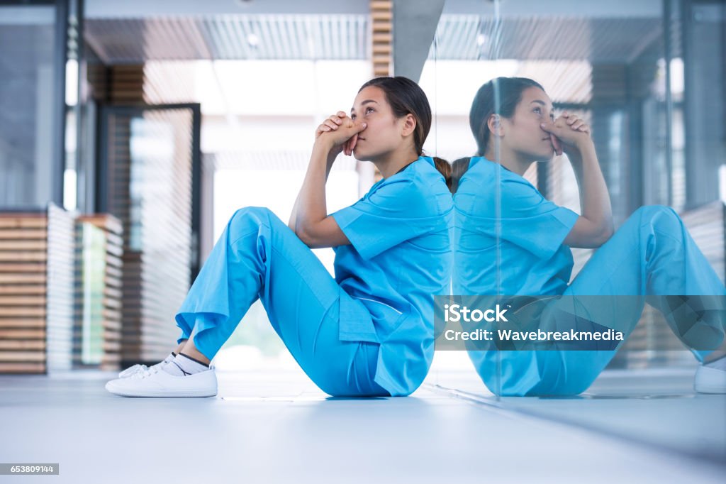 Worried nurse sitting on floor Worried nurse sitting in hospital corridor Nurse Stock Photo