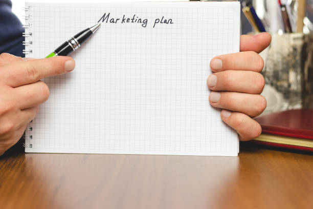 istock Hand with pen shows the text marketing plan in notepad at the table. Space for text. 653810316