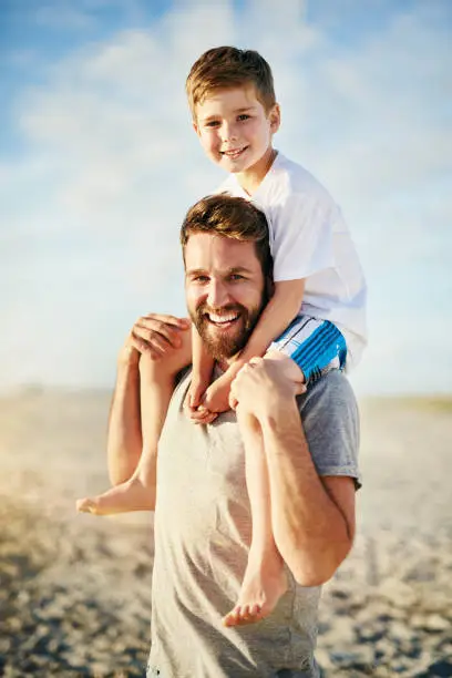 Portrait of a happy father carrying his son on his shoulders on the beach