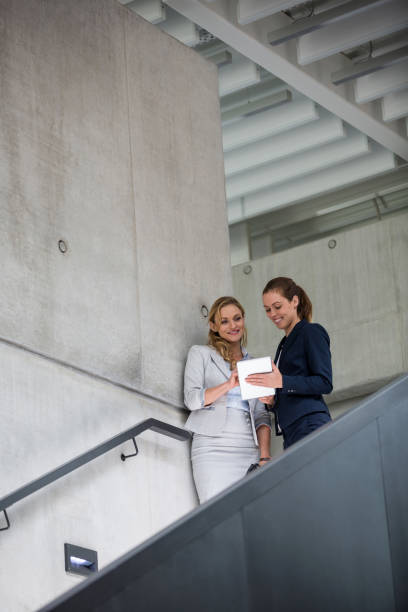 istock Businesswomen standing on staircase and using digital tablet 653817590