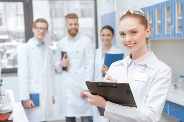 istock Young smiling woman scientist with clipboard standing near colleagues in lab 653826708
