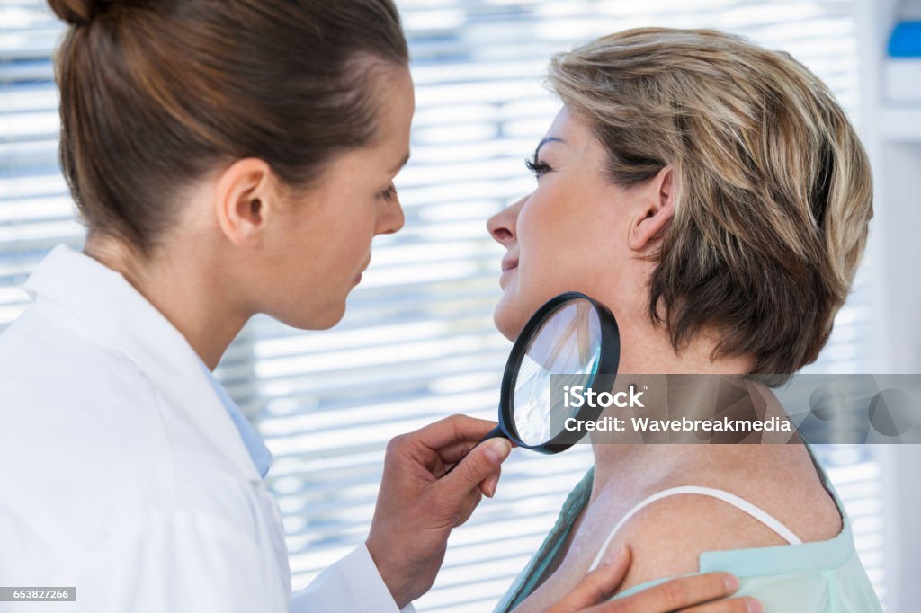 Dermatologist examining mole with magnifying glass Dermatologist examining mole with magnifying glass in clinic Skin Cancer Stock Photo