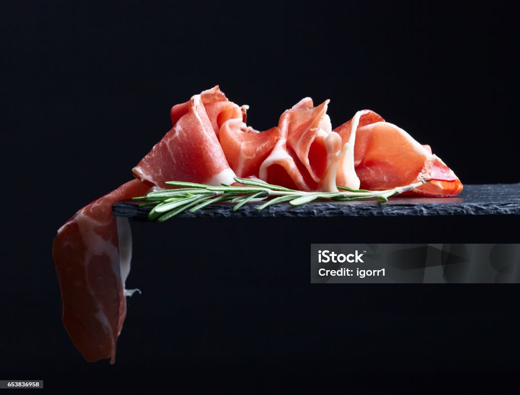 prosciutto with rosemary on a black  background prosciutto with rosemary on a black reflective background Serrano Ham Stock Photo