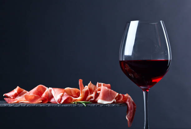 prosciutto with rosemary and red wine on a black  background prosciutto with rosemary and glass of red wine on a black  background prosciutto stock pictures, royalty-free photos & images