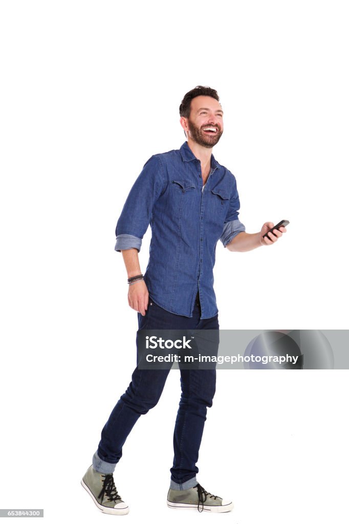 Handsome mature man walking with mobile phone and laughing Full length portrait of handsome mature man walking with mobile phone and laughing over white background Men Stock Photo