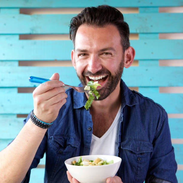 ritratto di uomo allegro che mangia insalata - man eating foto e immagini stock