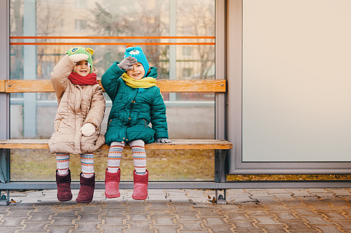 two little girls are sitting at the bus stop in the spring