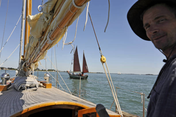 istock Classic wooden yacht; view forward with sailor looking at camera. 653854034