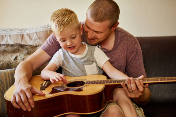 Time for another guitar lesson with Dad Cropped shot of a father and his little son playing the guitar together at home father and son guitar stock pictures, royalty-free photos & images