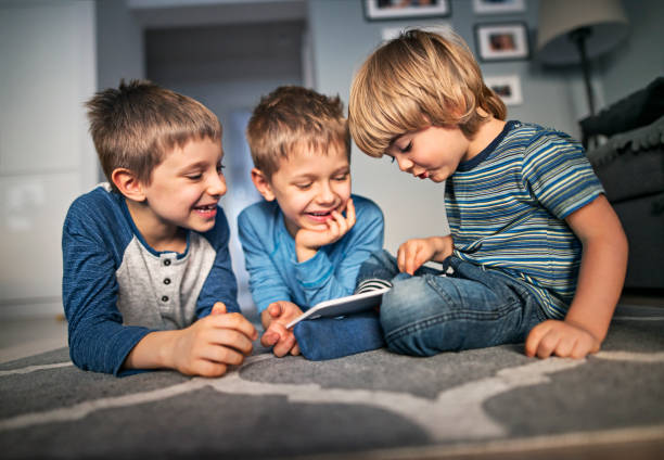 petits garçons jouant avec tablette numérique à la maison - three boys photos et images de collection