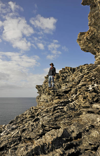 istock Man sitting on edge of cliff overlooking sea. 653863420