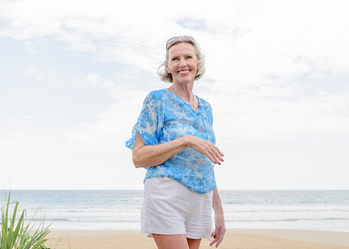 Woman in her 70s wearing blue blouse and white shorts, looking away with cheerful expression