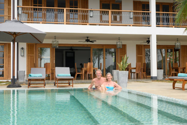 istock Senior couple on steps in swimming pool, smiling towards camera 653867254